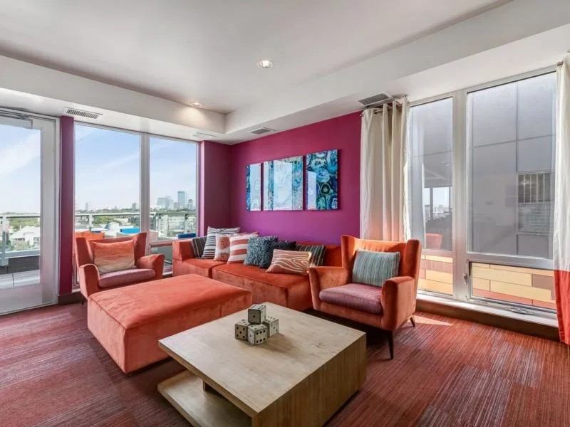 Stylish communal lounge with orange seating, a coffee table with dice decor, and large windows overlooking a city skyline.