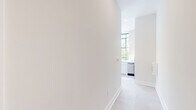 Located in the heart of downtown Winston-Salem, this thoughtfully designed 2-bedroom, 1-bathroom residence offers a compelling blend of modern finishes and architectural character. The most striking feature is a dramatic curved wall of floor-to-ceiling windows in the living area, framed in warm wood tones, that floods the space with natural light and offers lush tree-lined views of the surrounding streetscape. Recessed lighting complements the abundant natural light throughout.

The open kitchen is outfitted with white cabinetry, stainless steel appliances, and large windows with black steel framing, adding an urban, contemporary edge. Light-toned tile flooring runs throughout, lending a cohesive and clean aesthetic to the entire unit.

Both bedrooms are bright and simply finished with neutral walls and large windows — one bedroom features elevated clerestory-style windows with views of the Winston-Salem skyline, adding a distinct urban character. The hallway connects the rooms efficiently, with a dedicated closet providing additional storage.

The bathroom is elegantly appointed with wide-plank tile flooring, white cabinetry with matte black hardware, a clean-lined vanity with a stone countertop, and gold-toned accents. The overall ambiance is light, airy, and modern — ideal for urban living.