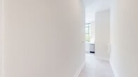 Located in the heart of downtown Winston-Salem, this thoughtfully designed 2-bedroom, 1-bathroom residence offers a compelling blend of modern finishes and architectural character. The most striking feature is a dramatic curved wall of floor-to-ceiling windows in the living area, framed in warm wood tones, that floods the space with natural light and offers lush tree-lined views of the surrounding streetscape. Recessed lighting complements the abundant natural light throughout.

The open kitchen is outfitted with white cabinetry, stainless steel appliances, and large windows with black steel framing, adding an urban, contemporary edge. Light-toned tile flooring runs throughout, lending a cohesive and clean aesthetic to the entire unit.

Both bedrooms are bright and simply finished with neutral walls and large windows — one bedroom features elevated clerestory-style windows with views of the Winston-Salem skyline, adding a distinct urban character. The hallway connects the rooms efficiently, with a dedicated closet providing additional storage.

The bathroom is elegantly appointed with wide-plank tile flooring, white cabinetry with matte black hardware, a clean-lined vanity with a stone countertop, and gold-toned accents. The overall ambiance is light, airy, and modern — ideal for urban living.