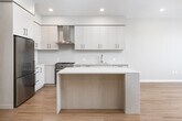 This contemporary single-floor residence showcases a clean, modern design with warm hardwood flooring that flows consistently throughout the open-concept living spaces. The kitchen is a standout feature, offering light wood flat-panel cabinetry extending to the ceiling, a marble-toned quartz countertop, a sleek stainless steel gas range with a metallic hood, a built-in wine cooler, and a generous island that doubles as a casual dining and prep surface. Recessed lighting illuminates the kitchen and living area, which opens toward expansive floor-to-ceiling windows that frame sweeping panoramic views, filling the space with abundant natural light.

The bedroom area is well-proportioned and connects to a custom-built walk-in closet featuring dark wood shelving, multiple hanging rails, and ample storage. A secondary bathroom offers a floating vanity with light wood cabinetry and a backlit mirror above a clean white sink, finished with neutral tile flooring. The primary bathroom is notably spacious, featuring a dual-sink floating vanity with a wide, illuminated mirror, a freestanding soaking tub, and a glass-enclosed walk-in shower, all finished in a refined, light neutral palette. The overall ambiance is polished and contemporary, with a cohesive design language throughout.