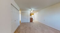 This single-floor unit is designed with a practical, open layout that connects the living area directly to the kitchen, creating a cohesive and functional flow throughout the space. The living area is finished with neutral wall-to-wall carpeting and features a ceiling fan with integrated lighting, providing both comfort and illumination. A set of double bifold closet doors along one wall offers convenient storage, while a separate door provides access to additional areas of the unit. Baseboard heating and a wall-mounted air conditioning unit ensure year-round climate control, and a window allows natural light to brighten the room.

The kitchen is positioned at one end of the open plan and is equipped with warm oak cabinetry, laminate countertops, and white appliances including an electric range, dishwasher, and refrigerator. A range hood is installed above the stove, and tile flooring distinguishes the kitchen from the carpeted living spaces.

The bedroom is a generously sized, carpeted room featuring its own ceiling fan, a window with natural light, and a wide built-in closet complete with a hanging rod and integrated shelving for organized storage.

The bathroom includes a full-size soaking tub with an overhead shower, a white surround with built-in shelving, and clean, simple fixtures throughout.