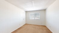 This single-floor unit offers a practical and efficient layout across three bedrooms, one bathroom, a kitchen, a utility room, and a closet. The interior features a clean, neutral color palette throughout, with white walls and light-toned finishes that create a bright, airy feel.

The galley-style kitchen is well-organized, featuring light wood cabinetry on both sides, gray laminate countertops, tile flooring, and white appliances including an electric range and a full-size refrigerator. A visible electrical panel is tucked neatly into the kitchen corridor, and the layout opens into the main living area.

The bedrooms are carpeted in warm beige tones and are bathed in natural light through horizontal-blind-fitted windows. The spacious primary bedroom offers generous room for furnishings, while the additional bedrooms provide comfortable accommodations with closet access. One bedroom features a sliding-door closet with a hanging rod, ideal for storage.

The bathroom is clean and straightforward, equipped with a full tub-shower combo surrounded by white tile, a toilet, and tile flooring. The unit also includes a dedicated utility room and additional closet space, enhancing overall storage capacity. The layout flows efficiently, making the most of the available footprint in a well-maintained, move-in-ready setting.