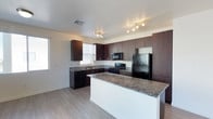 This single-floor residence offers a thoughtfully designed living space anchored by a standout kitchen. The kitchen is outfitted with rich, dark espresso-toned cabinetry that extends floor to ceiling, providing generous storage throughout. Granite countertops in warm earth tones add a polished, durable work surface, and the central kitchen island offers additional prep and gathering space. Black appliances — including a gas range, refrigerator, and dishwasher — complement the dark cabinetry for a cohesive, contemporary aesthetic. Track lighting and recessed fixtures illuminate the space efficiently, while multiple windows invite natural light to brighten the interior. The light hardwood-style flooring runs seamlessly throughout, creating a clean and modern foundation that ties the space together. The layout is open and functional, with the kitchen flowing naturally into the surrounding living areas. The overall ambiance is modern and practical, with quality finishes that balance style and everyday usability. This residence provides a comfortable, well-equipped environment suited for a variety of lifestyles.