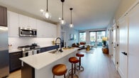 This single-floor residence is designed with a contemporary open-concept layout that seamlessly connects the kitchen, dining, and living areas. The kitchen is a standout feature, equipped with stainless steel appliances including a gas range, built-in microwave, and French door refrigerator. Two-toned cabinetry — crisp white uppers paired with deep navy lowers — frames a white quartz waterfall island with an integrated sink and matte black fixtures. Pendant globe lights with black metal accents hang overhead, adding a modern touch. Light wood-style flooring flows throughout the main living areas, enhancing the bright, airy atmosphere.

The living room opens directly to a private outdoor patio through full-length glass doors, allowing abundant natural light and outdoor views. The space accommodates a generous sectional seating arrangement centered around a round accent table.

The bedrooms are well-proportioned, each featuring large windows with exterior views, neutral-toned walls, and plush carpeting. The primary bedroom includes direct patio access. The bathroom features a walk-in glass-enclosed shower with white subway tile walls and matte black hardware, offering a clean, modern aesthetic throughout.