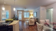 This single-floor residence is thoughtfully designed with a cohesive neutral palette and warm wood-look flooring that flows throughout the main living areas. The open-concept living room is bright and welcoming, featuring a ceiling fan, large windows with horizontal blinds that invite natural light, and a front entry door with a transom window above. The space transitions seamlessly into a dedicated dining area and a well-equipped kitchen. The kitchen features dark espresso cabinetry, granite-style countertops, black appliances including a refrigerator, microwave, dishwasher, and stovetop, along with a functional peninsula that adds additional prep and seating space. An in-unit washer and dryer are conveniently tucked nearby. The primary bedroom offers plush carpeting, a ceiling fan, and a window for natural light, leading to an en-suite bathroom with a double-sink vanity, dark cabinetry, wood-look flooring, and a shower-tub combination. A generously sized walk-in closet with wire shelving provides ample storage. The second bedroom is equally comfortable, with soft carpeting and its own bathroom featuring a shower and dark vanity. The overall ambiance is warm, functional, and move-in ready.