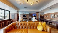 Located at 360 Acoma Street in Denver's vibrant Baker neighborhood, the Parlor Room is a thoughtfully designed social lounge that blends classic sophistication with modern comfort. The single-floor space offers a generous, open layout that accommodates a variety of social settings and activities.

At the heart of the room is a full-service bar, outfitted with draft taps, stainless steel appliances, open wood shelving, and a large wall-mounted TV — ideal for gathering during events or game days. Bar-height seating lines the counter, providing ample space for guests. A billiards table anchors the entertainment zone, complemented by additional mounted screens and warm wood-paneled walls that lend a refined, club-like atmosphere.

The lounge area is anchored by richly tufted caramel leather sofas and accented with vibrant yellow throw pillows and a colorful floral area rug. A sculptural wood coffee table adds an artistic focal point. Built-in bench seating along the walls offers additional relaxed gathering spots.

Ornate ceiling medallions with Edison bulb pendant lighting add a vintage-inspired elegance overhead, while tongue-and-groove ceiling detail enhances the architectural character. A sun-drenched sunroom extension features floor-to-ceiling windows and glass doors that open to an outdoor terrace, flooding the space with natural light and offering views of the surrounding courtyard — creating a seamless indoor-outdoor connection throughout.