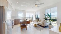 Located at 1017 Lake Ave in Lake Worth Beach, FL, this single-floor residence showcases a clean, contemporary design defined by crisp white walls, large-format tile flooring, and an abundance of natural light throughout. The open-concept living and kitchen area serves as the heart of the unit, where floor-to-ceiling black-framed windows frame sweeping elevated views of the surrounding Lake Worth Beach landscape. A ceiling fan overhead and roller shades provide comfort and light control, while a balcony accessible from the living area extends the living space outdoors.

The kitchen is thoughtfully designed with a two-tone palette of white upper cabinetry and warm wood-grain lower cabinets, complemented by a subway tile backsplash and stainless steel appliances. A central island with a white countertop offers casual seating and additional workspace.

Two bedrooms provide comfortable retreats; the primary bedroom benefits from large windows with outdoor views and connects to a well-appointed en-suite bathroom featuring a glass-enclosed walk-in shower, a long wood-grain vanity, and clean tile flooring. A second full bathroom with a shower-tub combination serves the additional bedroom. A bright hallway connects all areas, reinforcing the unit's cohesive, airy aesthetic throughout.