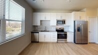 This single-floor unit offers a clean, contemporary design with consistent light wood-tone flooring throughout, creating a cohesive and airy feel across all spaces. The open-concept kitchen and living area serves as the heart of the unit, where a well-designed kitchen is outfitted with crisp white shaker cabinetry, granite countertops, a subway tile backsplash, and a full suite of stainless steel appliances including a refrigerator with ice and water dispenser, electric range, over-the-range microwave, and dishwasher. A large window in the adjacent living area floods the space with natural light and provides views of the surrounding greenery. The bedroom continues the bright, open aesthetic, featuring a ceiling fan, ample wall space, and a generously sized window with outdoor views. The bathroom is thoughtfully finished with granite countertops on the vanity, a large wall mirror, a soaking tub with a shower, and striking marble-patterned tile surround, complemented by a recessed wall niche and a tall white storage cabinet. Throughout the unit, neutral wall tones and recessed lighting contribute to a modern, move-in-ready atmosphere.