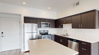 This thoughtfully designed one-bedroom, one-bathroom residence offers a clean, modern aesthetic across a single floor. The open-concept layout connects the kitchen and living area seamlessly, creating an efficient and inviting flow throughout the space.

The kitchen is a standout feature, showcasing rich dark-toned cabinetry that extends to the ceiling for generous storage, complemented by sleek light quartz countertops and a full suite of stainless steel appliances, including a refrigerator, electric range, microwave, and dishwasher. A central kitchen island with bar seating serves as a natural gathering point and adds valuable counter space. Light wood-style flooring grounds the kitchen and living area with a warm, contemporary feel.

The bedroom is a comfortable, carpeted retreat featuring a ceiling fan, a window with an exterior view, and neutral walls that create a calm atmosphere. The bathroom continues the design language of the rest of the home, with dark wood cabinetry, a white countertop vanity, a large mirror, and wood-look tile flooring. A closet and dedicated entrance round out the functional layout, adding practical storage and a defined arrival space to this well-organized residence.