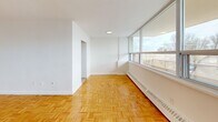 Located at 1130 Wilson Ave in Toronto's Wilson Heights neighbourhood, this 2-bedroom, 1-bathroom unit offers a functional and well-organized layout across a single floor. The consistent use of warm-toned parquet flooring throughout creates a cohesive and inviting atmosphere in every room.

The spacious living room is a standout feature, boasting a floor-to-ceiling window wall that floods the space with natural light and offers open views of the surrounding cityscape. Baseboard heating runs along the windows, ensuring year-round comfort. The clean white walls provide a neutral canvas throughout the unit.

The primary bedroom is generously sized, offering ample room for furnishings, and benefits from its own window with city views and baseboard heating. The second bedroom is also well-proportioned with a bright, airy feel and private access through a white interior door.

The bathroom is finished with large-format ceramic wall tiles accented by a decorative mosaic border strip, and features a full soaker tub with an overhead shower. A dedicated closet and hallway contribute to practical storage and smooth circulation throughout the unit.

Overall, the space presents a clean, classic aesthetic with durable finishes and an abundance of natural light, making it a comfortable and functional urban residence.