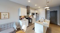 This single-floor residence offers a thoughtfully designed layout that maximizes functionality within a compact footprint. The interior is finished with neutral gray walls and light flooring throughout, creating a cohesive and modern aesthetic.

The kitchen is a standout feature, outfitted with crisp white shaker-style cabinetry, granite countertops, and a full suite of stainless steel appliances, including a range with an overhead stainless hood, built-in microwave, and a full-size refrigerator. A tile backsplash adds texture, while a peninsula with a sink and pendant lighting overhead provides additional prep space and casual seating. Recessed lighting illuminates the area effectively.

The living area is carpeted and receives natural light through a window overlooking the exterior. The space accommodates a comfortable seating arrangement and connects directly to the bedroom, which benefits from the same soft carpeting and neutral palette.

The bathroom is clean and functional, featuring a full tub-shower combination with chrome fixtures and a toilet, finished with light tile flooring. The overall design of the residence prioritizes a modern, move-in ready feel with consistent finishes throughout.