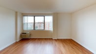 This single-floor unit is finished with warm hardwood-style flooring that runs consistently throughout the main living areas, creating a cohesive and clean aesthetic. The main living space is bright and open, anchored by a large multi-pane window that fills the room with natural light and offers views of the surrounding urban landscape. A wall-mounted HVAC unit provides in-unit climate control.

The kitchen is thoughtfully appointed with rich medium-toned wood cabinetry, a bold mosaic tile backsplash featuring a mix of gray tones, dark granite-style countertops, and a black gas range, giving the space a modern, functional character.

The bathroom features a dark granite vanity top with an undermount sink, a framed mirror, a dark wood medicine cabinet with storage above the toilet, and tile detailing near the shower area, creating a polished and practical space.

Storage is a notable feature of this unit, with a walk-in closet equipped with wire shelving systems, as well as an additional built-in shelving closet off the secondary room. The hallway leads efficiently between rooms, maintaining a logical and practical layout throughout.