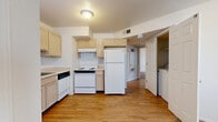 This single-floor residence offers a practical and well-organized layout designed for comfortable everyday living. The kitchen serves as a central functional hub, outfitted with light natural wood cabinetry providing generous upper and lower storage, a double-basin sink, laminate countertops, and white appliances including a refrigerator, electric range, and dishwasher. Wood-look flooring runs throughout the kitchen and connecting areas, lending warmth and ease of maintenance. A dedicated laundry closet is conveniently accessible directly from the kitchen area, housing a washer and dryer. The bedrooms are carpeted for comfort and include ceiling fans for climate control, natural light from windows with blinds, and built-in closets offering organized storage. The electrical panel is also neatly housed within the unit. Two bathrooms serve the residence: one features a full tub-shower combination with a single-sink vanity framed in matching light wood cabinetry and a large mirror, while the second bathroom offers a similar vanity setup with additional wall-mounted cabinetry. Both bathrooms continue the wood-look flooring seen in the main living areas. Overall, the space maintains a clean, neutral palette with white walls and light wood tones throughout, creating a bright and cohesive atmosphere.