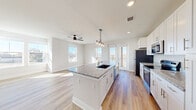 This well-appointed single-floor residence offers four bedrooms and three bathrooms thoughtfully arranged across a comfortable footprint. The open-concept kitchen and living area serves as the heart of the home, featuring white shaker cabinetry, granite countertops, a central island with an undermount sink, pendant lighting, and stainless steel appliances. Large windows and a glass door lead to a private balcony, flooding the space with natural light and offering outdoor views. A ceiling fan completes the living area, enhancing both comfort and airflow.

Light-toned hardwood flooring runs throughout the main living areas and hallways, while plush carpeting adds warmth to the bedrooms. The primary bedroom is a generous retreat, benefiting from multiple windows, a ceiling fan, and direct access to a spacious walk-in closet with wire shelving. The primary bathroom features a double-sink vanity with granite countertops, white shaker cabinetry, and hardwood-style flooring. Additional bedrooms are carpeted and receive ample natural light through well-positioned windows. A wide, clean hallway connects the rooms, reinforcing the home's organized and airy layout. The overall design is modern and neutral, creating a bright, move-in-ready environment.