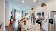 This single-story, one-bedroom, one-bathroom unit offers a thoughtfully designed open-concept layout that maximizes its generous footprint. The kitchen serves as a central feature, showcasing white shaker cabinetry, granite countertops, a subway tile backsplash, and a full suite of stainless steel appliances including a side-by-side refrigerator, electric range, and built-in microwave. A freestanding center island with seating provides additional prep space and a natural gathering point that flows seamlessly into the living area.

The living room is bright and welcoming, featuring wood-style plank flooring, a ceiling fan, and a large sliding glass door that opens to a private balcony, filling the space with natural light and outdoor views. A built-in desk nook adds functional workspace just off the main living area.

The bedroom is carpeted and well-lit by a large window framing outdoor views. It offers a calm, comfortable retreat with ample room for furnishings. The bathroom is finished with granite countertops and wood-style flooring consistent with the rest of the unit. Throughout, clean white walls, recessed lighting, and modern five-panel interior doors contribute to a cohesive, contemporary aesthetic.