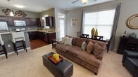This single-story residence offers a thoughtfully designed open-concept layout that seamlessly connects the living, dining, and kitchen areas. The living room features warm hardwood-style flooring near the entryway, transitioning to plush carpet in the main seating area. A ceiling fan with integrated lighting anchors the space, while large windows with blinds and curtain panels allow generous natural light to flow through. The front door includes a transom window above, adding to the bright, welcoming atmosphere.

The kitchen is well-equipped with rich dark cabinetry, granite countertops, stainless steel appliances including a gas range, built-in microwave, and dishwasher, along with a double-basin sink beneath a window. A pendant light adds a refined touch overhead.

The bedroom is a comfortable retreat finished in neutral tones with soft carpet, a window overlooking greenery, and a spacious walk-in closet outfitted with wire shelving for ample storage. Two full bathrooms are present — one with cool blue-gray walls and the other in warm tan tones — each featuring a tub/shower combination with tile surround. A dedicated laundry room houses a full-size washer and dryer alongside a water heater, completing this functional and cohesive home.