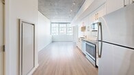 Located in the heart of Seattle's First Hill neighborhood, this thoughtfully designed unit offers a sleek, modern aesthetic throughout. The open-plan living and kitchen area is a standout, featuring an exposed concrete ceiling with track lighting that adds an industrial-chic character. Light hardwood-style flooring extends across the main living space, reflecting natural light that pours in through large floor-to-ceiling windows offering expansive city views of the Seattle skyline.

The kitchen is efficiently laid out along one wall, outfitted with white cabinetry featuring gold-toned hardware, stainless steel appliances including a range, microwave, dishwasher, and refrigerator, as well as a pantry for additional storage. The space flows seamlessly into the open living area, making it ideal for everyday living.

The bedroom is carpeted for comfort and features a large window framing striking urban views, along with an exposed concrete ceiling that ties back to the industrial design theme. Two closets provide ample storage throughout the unit. A long entry hallway with recessed lighting connects the spaces with clean, white walls.

The bathroom is finished with white subway tile surrounding a full soaking tub and shower combo, complemented by hardwood-style flooring and a vanity, delivering a clean and functional design.