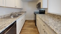 This single-floor residence offers a clean, modern aesthetic carried consistently throughout its layout. The living area is bright and open, benefiting from abundant natural light streaming through large sliding glass doors fitted with vertical blinds, creating an airy and welcoming atmosphere. The wood-style flooring runs seamlessly across the living spaces, lending warmth and visual continuity.

The galley-style kitchen is well-equipped and thoughtfully designed, featuring granite countertops, crisp white cabinetry with brushed nickel hardware, and stainless steel appliances including a range, microwave, and dishwasher. The double-basin sink and generous counter space make it both functional and attractive.

The bedrooms are comfortably sized, each bathed in natural light from windows with blinds. One bedroom features a full wall of sliding closet doors, offering excellent built-in storage. The neutral wall tones and wood-style flooring in the bedrooms create a calm, restful environment.

The bathrooms are finished to match the overall design language of the home, with granite-topped vanities, white cabinetry, and tiled tub-shower combinations. The beige tile surround in the bathrooms adds a classic, understated touch. Overall, the space presents a cohesive, move-in-ready interior with modern updates and a neutral palette throughout.