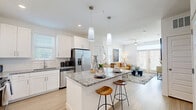 This thoughtfully designed single-story residence offers 1 bedroom and 2 bathrooms within a smartly utilized floor plan. The open-concept kitchen and living area serves as the heart of the home, where light hardwood flooring flows throughout. The kitchen is outfitted with crisp white shaker cabinetry, granite countertops, a full suite of stainless steel appliances, and a central island with bar seating, illuminated by elegant pendant lighting — ideal for both cooking and casual dining. The kitchen opens seamlessly into the living room, which features large windows and French doors that invite an abundance of natural light and provide outdoor access. A ceiling fan adds comfort to the airy space. The bedroom is a serene retreat, carpeted for warmth, with wide windows that allow natural light to filter through sheer curtains. The primary bathroom connects directly to a walk-in closet, and features granite countertops, white cabinetry, and wood-look flooring. A dedicated closet provides additional storage. The overall aesthetic is clean and contemporary, with a bright, neutral palette that creates a welcoming and cohesive atmosphere throughout the home.