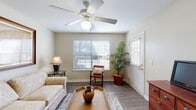 This single-floor residence offers a cohesive and comfortable layout designed for easy everyday living. The living room serves as a welcoming centerpiece, featuring wood-look flooring, a ceiling fan with light fixture, multiple windows fitted with horizontal blinds that allow natural light to filter in, and a direct access door to the exterior. The space is open and functional, connecting naturally to the rest of the home.

The dining area is distinguished by an elegant wrought-iron chandelier and wainscoting along the lower walls, lending the room a refined character. A hallway lined with open cube shelving provides both storage and visual interest, connecting the main living spaces to the rest of the unit.

The kitchen is bright and practical, outfitted with white raised-panel cabinetry, white countertops, a double-basin sink, a dishwasher, and additional appliances. Its clean, neutral palette keeps the space feeling fresh and organized.

The bedroom is a serene retreat, carpeted for comfort and centered around a striking four-poster wicker and wood bed frame. A ceiling fan overhead, bedside lamps, and flanking nightstands complete the room. An en-suite bathroom is accessible directly from the bedroom and features a vanity with white cabinetry, a shower-tub combination, and wood-look flooring. A second full bathroom is also accessible from the main hallway, providing added convenience.