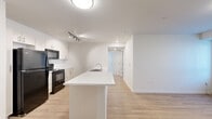Located at 5886 Tutt Blvd in Colorado Springs, CO, this 2-bedroom, 2-bathroom unit offers a well-designed single-floor layout with a clean, contemporary aesthetic. The open-concept kitchen and living area forms the heart of the home, anchored by a sleek white peninsula with an integrated sink — ideal for casual dining or meal prep. The kitchen is equipped with black appliances, including a refrigerator, electric range, and over-the-range microwave, complemented by white cabinetry and track lighting overhead. Light wood-style flooring flows throughout the main living areas, creating a warm and cohesive look. The living area is bright and open, with a door leading to an exterior access point and a window dressed with vertical blinds, allowing for natural light. Both bedrooms are carpeted and generously proportioned, with the primary bedroom offering ample space and access to a closet. Each room features vertical blind-covered windows and wall-unit climate control. The two bathrooms are finished in a clean, all-white palette, with one featuring a full tub-shower combination and light wood-style flooring. A dedicated closet provides additional storage. The overall ambiance is fresh, neutral, and move-in ready, suited for comfortable everyday living.