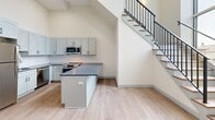 Located at 160 Seabury St in Fall River, MA, this two-bedroom, two-bathroom two-story unit showcases a thoughtful blend of historic architectural character and modern interior finishes. The main floor serves as the primary living level and offers generous square footage, anchored by a kitchen featuring gray shaker-style cabinetry, granite countertops, a subway tile backsplash, and stainless steel appliances including a range and microwave. A peninsula provides additional prep and seating space. Light wood-tone flooring runs throughout, complementing the neutral, cream-toned walls. A sleek staircase with a metal railing rises from the main floor to the upper level, which houses the remaining bedroom and additional hallway space.

A distinctive arched doorway with a warm wood door adds architectural character to the entry, and exposed ductwork provides an industrial accent while maintaining a clean aesthetic. Both bathrooms are finished with hexagonal tile flooring, gray vanity cabinetry, granite countertops, and large mirrors. One bathroom includes a glass-enclosed walk-in shower. The bedrooms feature light hardwood flooring and ample closet space, with one bedroom including a sliding double-door closet. Windows throughout allow natural light to filter in, contributing to the unit's bright, fresh ambiance.