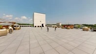 Located at 245 King St in Port Chester, NY, this rooftop terrace offers a thoughtfully designed outdoor amenity space that combines functionality with a modern aesthetic. The terrace is finished with large-format light gray pavers that extend across a generous open deck, providing a clean, contemporary look underfoot.

A standout feature of the rooftop is its extensive living green roof sections, planted with a lush variety of sedum and ground-cover plants in rich hues of green, amber, and red. These eco-friendly installations are bordered by sleek dark-toned planters and white parapet walls, contributing both visual interest and environmental value.

The terrace is well-equipped for outdoor entertaining, featuring multiple BBQ grilling stations positioned along one side, alongside a dedicated lounge area furnished with comfortable seating arrangements. Slim, modern bollard-style fixtures are distributed across the deck, adding subtle architectural detail.

From virtually every vantage point on the rooftop, residents enjoy sweeping panoramic views of the Port Chester skyline and the surrounding residential and commercial neighborhood, with mature treetops and open sky completing the backdrop. The abundance of natural light and open sky above creates an airy, expansive atmosphere, making this rooftop terrace an inviting destination for relaxation and social gatherings alike.