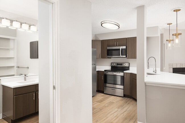 Modern apartment kitchen with elegant white countertops, stainless steel appliances, and warm wood flooring. - Avana Belmar