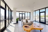 Located at 110 W Ocean Blvd in downtown Long Beach, California, this impressive rooftop space offers a sophisticated blend of interior comfort and open-air living. The generously proportioned living room is defined by floor-to-ceiling black-framed glass walls and sliding doors that flood the interior with natural light while framing panoramic views of the Long Beach skyline. Clean white ceilings with recessed lighting, smooth concrete-finish flooring, and crisp white columns contribute to a modern, minimalist aesthetic. A standout live-edge wood coffee table adds a natural, organic contrast to the contemporary surroundings, anchoring the seating area with character and warmth.

Multiple access points lead from the living room directly to the surrounding outdoor terraces, which are finished with wood-tone deck tiles and designed for versatile use. These exterior spaces feature dedicated lounge seating, dining areas, and large planter vessels with greenery, creating an al fresco environment ideal for entertaining. Lush vertical hedging provides privacy along portions of the perimeter, while open sightlines deliver unobstructed views of the downtown cityscape and beyond. The overall ambiance is bright, airy, and distinctly urban — a refined rooftop retreat in the heart of Long Beach.