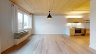This thoughtfully designed single-floor unit showcases a contemporary aesthetic anchored by striking exposed wood plank ceilings that run throughout, lending warmth and architectural character to the space. Light hardwood flooring flows seamlessly across the main living and kitchen areas, complementing the clean white walls and creating a bright, airy atmosphere.

The open living area is generously proportioned, featuring large windows that invite natural light and a bold pendant light fixture that serves as a focal point. A wall-mounted HVAC unit ensures year-round comfort.

The kitchen is well-appointed with light maple cabinetry, white tile backsplash, and a full suite of stainless steel appliances including a side-by-side refrigerator with water dispenser, electric range, dishwasher, and under-cabinet range hood. Open stainless steel shelving adds a modern, functional touch alongside ample upper and lower cabinet storage.

The bedroom features plush carpeted flooring, a wall sconce for ambient lighting, and a window overlooking the exterior. An additional room with hardwood flooring and a ceiling-mounted clothing rod offers flexible use as a second bedroom or den.

The bathroom is spacious and accessible, finished with light wood-toned floating vanity cabinetry, a large mirror, white countertops, and grab bars, reflecting a thoughtful and inclusive design approach throughout.
