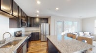 This single-floor residence offers a thoughtfully designed layout with a cohesive blend of modern finishes and functional living spaces. The kitchen serves as a central highlight, showcasing rich dark cabinetry, light granite countertops, and a full suite of stainless steel appliances including a refrigerator, range, and over-the-range microwave. A generous island with matching granite provides additional prep and dining space, while warm hardwood flooring and recessed lighting complete the kitchen's polished look. A sliding glass door allows natural light to pour in, connecting the kitchen to the adjacent living area. The hallway, finished with smooth hardwood flooring and crisp white walls, connects the living areas to the private quarters, offering a clean and open corridor with recessed lighting overhead. The bedrooms are comfortably scaled, each featuring plush carpeting, neutral wall tones, and large windows that invite ample natural light and outdoor views. The bathroom is appointed with a dual-sink vanity featuring dark cabinetry, a wide mirror, and a classic black-and-white mosaic tile floor, adding a timeless aesthetic detail. Overall, the space presents a well-balanced combination of contemporary design and comfortable living across its single level.