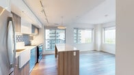 Located on the 17th floor at 50 High Park Ave in Toronto's vibrant High Park neighbourhood, this two-bedroom, two-bathroom unit offers a well-designed layout with modern finishes throughout. Light-toned wood-style flooring flows through the open-concept living and dining area, creating a bright and cohesive feel. The kitchen is a standout feature, equipped with stainless steel appliances, a central island with built-in shelving, pendant lighting, and a decorative patterned tile backsplash — all complemented by warm wood cabinetry and clean white countertops. Both bedrooms are finished with the same light flooring, crisp white walls, and generous closet space. The primary bedroom enjoys large floor-to-ceiling windows that frame sweeping city views, filling the room with natural light. The two bathrooms are finished with large-format floor tiles, white fixtures, and warm wood-accented vanities. One bathroom features a tiled walk-in shower, while the other offers a soaker tub with brushed gold hardware. A hallway connects all rooms efficiently, and the overall layout makes thoughtful use of every square foot. The unit's high-floor position provides elevated city and treetop views, contributing to a calm and airy urban living experience.