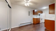 This single-floor unit offers a functional and well-appointed layout with distinct living, sleeping, and kitchen zones. The galley-style kitchen is a standout feature, showcasing warm medium-toned wood cabinetry paired with marble-look countertops that run along both sides, providing generous prep space. Dark hardwood-style flooring runs through the kitchen and entry areas, adding contrast and warmth. White appliances, including a range and refrigerator, complement the clean aesthetic, while a ceiling fan with integrated lighting overhead adds practicality.

The living area is generously proportioned, featuring neutral carpet, soft gray walls, and a large window that fills the room with natural light and offers views of surrounding greenery. A baseboard heating system runs along the perimeter, ensuring comfort throughout. The bedroom mirrors this inviting ambiance, with carpeted flooring, a ceiling fan, a wall-mounted AC unit, a baseboard heater, and a mirrored sliding closet that enhances the sense of space. A window provides additional natural light and outdoor views.

The bathroom is finished with full white ceramic tile surrounding the tub and shower, complemented by neutral tile flooring, creating a clean and classic look. An entry hallway with a mirrored closet connects the spaces seamlessly.