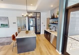 The Argenta Townhomes Club House is a 1,360 square foot single-story facility designed to serve as a central gathering and amenity space for residents. The interior showcases a contemporary open floor plan with distinct functional zones. 

Upon entry, visitors are greeted by a bright, airy lounge area featuring comfortable leather sofas, stylish accent chairs, and a modern coffee table. Large windows with teal trim flood the space with natural light and offer views of the townhome community.

Adjacent to the lounge is a sleek kitchen area with stainless steel appliances, quartz countertops, and a central island, perfect for casual dining or social gatherings. The space seamlessly transitions into a multi-purpose area that can serve as a meeting room or workspace, equipped with a wooden desk and ergonomic chairs.

The clubhouse also boasts a state-of-the-art fitness center, complete with cardio equipment, weight machines, and free weights. Mirrored walls and large windows create an open, energizing atmosphere for workouts.

Throughout the space, the design aesthetic is cohesive, featuring a neutral color palette with pops of teal and orange. Wood-look flooring, recessed lighting, and modern fixtures contribute to the overall contemporary ambiance. This well-appointed clubhouse serves as an extension of residents' homes, offering versatile spaces for relaxation, socializing, and wellness activities.
