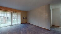 Located at 10145 W Cold Spring Rd in Greenfield, Wisconsin, this single-floor unit offers a practical and functional layout distributed across several well-defined living spaces. The living room is generously proportioned, featuring plush carpeting, neutral-toned walls, and a sliding glass door fitted with vertical blinds that allows natural light to filter in while providing access to an outdoor area. A ceiling fan adds to the comfort of the connected space, which flows openly toward additional rooms.

The galley-style kitchen is efficiently designed with dark wood cabinetry lining both sides, granite-look countertops, a stainless steel sink, and black appliances including a range and refrigerator. Tile flooring runs the length of the kitchen, and a louvered closet door at the far end provides additional storage.

The bedrooms are carpeted and neutral in tone, with one room featuring a louvered closet door and another offering access to what appears to be a walk-in closet area. A window brings in natural light, and a baseboard heating system runs along the wall. The bathroom includes a full-size tub and shower combination with clean white subway tile surround and chrome fixtures, offering a simple and functional design.