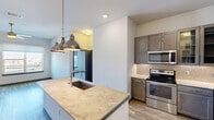 This thoughtfully designed 2-bedroom, 2-bathroom residence offers a modern, open-concept layout across a single floor. The kitchen serves as a central highlight, featuring a granite-topped island with an undermount sink, stylish industrial pendant lighting, taupe shaker-style cabinetry, a mosaic tile backsplash, and a full suite of stainless steel appliances including a French door refrigerator, electric range, and built-in microwave. Wood-look luxury vinyl plank flooring flows throughout the main living areas, creating a cohesive and contemporary feel. The living room is bright and airy, with a ceiling fan, a large window, and a glass door that opens to an outdoor view of the surrounding cityscape. Both bedrooms are carpeted and equipped with ceiling fans and roller shade windows that allow ample natural light. The primary bathroom is elegantly finished with a dual-sink vanity topped in granite, taupe cabinetry, wood-look tile flooring, a frameless glass walk-in shower, and a large mirror with vanity lighting. Each bedroom is paired with a closet, including a walk-in closet featuring built-in shelving and a hanging rod. A dedicated laundry area with a Whirlpool washer and dryer set, topped with a granite folding surface, adds everyday convenience to this well-equipped residence.