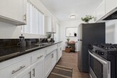 This 640-square-foot, one-bedroom, one-bathroom apartment is thoughtfully designed to maximize space and functionality across a single floor. The bright living room features light hardwood-style flooring, crisp white walls, and a sliding glass door that opens directly onto a private outdoor patio — ideal for seamless indoor-outdoor living. A wall-mounted air conditioning unit ensures year-round comfort. The kitchen is outfitted with white shaker cabinets, quartz countertops, a stainless steel double-basin sink, and a stainless steel gas range, all illuminated by a window overlooking greenery. The 130-square-foot primary bedroom offers a serene retreat with a wide window framing outdoor views, light-toned flooring, and ample wall space. The full bathroom includes a tub-shower combination with chrome fixtures and a window that brings in natural light. A hallway connects the main living areas efficiently, contributing to the unit's practical flow. Throughout the apartment, consistent light flooring and a neutral white palette create a clean, cohesive aesthetic that feels open and airy despite the compact footprint.