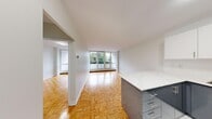 This well-designed one-bedroom, one-bathroom unit makes efficient use of its compact footprint across a single floor. The open living area is a standout feature, anchored by classic parquet wood flooring in a basket-weave pattern that extends throughout the main living spaces. Large floor-to-ceiling windows at the far end of the living area flood the space with natural light while framing views of surrounding greenery and neighbouring buildings, creating an airy, open atmosphere.

The kitchen is thoughtfully laid out with a peninsula that opens toward the living area, promoting an open-concept feel. It features two-tone cabinetry—grey lower cabinets paired with white uppers—white stone countertops, white tile flooring, a stainless steel sink, and stainless steel appliances including a refrigerator and range.

The bedroom is a well-proportioned private retreat, featuring the same warm parquet flooring, a large window with outdoor views, and a double-door closet providing ample storage. An additional door connects directly to the bathroom, which is finished with clean white tile and includes a full bathtub with shower. A hallway connects the key areas of the unit, contributing to a logical and functional layout throughout.