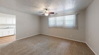 This 2-bedroom, 1-bathroom single-story unit offers a efficiently organized layout across a compact footprint. The living area features neutral-toned carpet, a textured ceiling, and a ceiling fan with light fixture, complemented by a large window dressed with vertical blinds that allows natural light to filter through. An open sightline connects the living space directly to the kitchen.

The kitchen is well-appointed with white cabinetry offering ample storage, gray laminate countertops, hardwood flooring, and white appliances including a gas range, refrigerator, and dishwasher. A stainless steel sink completes the functional workspace.

The spacious primary bedroom includes a ceiling fan, plush carpeting, a large window, and access to a dedicated walk-in closet with built-in shelving. The second bedroom similarly features carpet, a ceiling fan, and a window with vertical blinds. An additional room with hardwood flooring and a window provides flexible utility space.

The bathroom is straightforward, featuring hardwood-style flooring, a tub-shower combination with white tile surround, and clean white fixtures. The entryway transitions between hardwood and carpet flooring, with two doors providing entry and closet access, establishing a tidy transition into the living space.