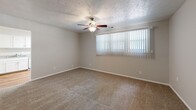 This 2-bedroom, 1-bathroom single-story unit offers a efficiently organized layout across a compact footprint. The living area features neutral-toned carpet, a textured ceiling, and a ceiling fan with light fixture, complemented by a large window dressed with vertical blinds that allows natural light to filter through. An open sightline connects the living space directly to the kitchen.

The kitchen is well-appointed with white cabinetry offering ample storage, gray laminate countertops, hardwood flooring, and white appliances including a gas range, refrigerator, and dishwasher. A stainless steel sink completes the functional workspace.

The spacious primary bedroom includes a ceiling fan, plush carpeting, a large window, and access to a dedicated walk-in closet with built-in shelving. The second bedroom similarly features carpet, a ceiling fan, and a window with vertical blinds. An additional room with hardwood flooring and a window provides flexible utility space.

The bathroom is straightforward, featuring hardwood-style flooring, a tub-shower combination with white tile surround, and clean white fixtures. The entryway transitions between hardwood and carpet flooring, with two doors providing entry and closet access, establishing a tidy transition into the living space.