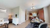 This three-floor townhouse offers a thoughtfully designed layout with two bedrooms and two and a half bathrooms. The main living level features an open-concept arrangement connecting the living room, dining area, and kitchen. The living room is bright and welcoming, with light hardwood-style flooring and a sliding glass door that floods the space with natural light and provides outdoor access. The adjacent dining area accommodates a full-sized dining table beneath an elegant chandelier, with a large window adding to the airy feel. The kitchen is well-equipped with rich cherry wood cabinetry, granite countertops, stainless steel appliances including a dishwasher, range, and microwave, plus a central island for added prep space. A half bath on the main level features a white vanity with dark granite countertop and tile flooring. Upstairs, the primary bedroom is generously sized with plush carpeting, a ceiling fan, and access to a walk-in closet. The second bedroom also offers comfortable proportions, a large window with outdoor views, and a full closet. A staircase with a pendant light fixture connects the floors gracefully. The lower level houses an attached garage and a utility area with a washer, dryer, and water heater.