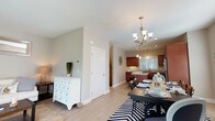 This three-floor townhouse offers a thoughtfully designed layout with two bedrooms and two and a half bathrooms. The main living level features an open-concept arrangement connecting the living room, dining area, and kitchen. The living room is bright and welcoming, with light hardwood-style flooring and a sliding glass door that floods the space with natural light and provides outdoor access. The adjacent dining area accommodates a full-sized dining table beneath an elegant chandelier, with a large window adding to the airy feel. The kitchen is well-equipped with rich cherry wood cabinetry, granite countertops, stainless steel appliances including a dishwasher, range, and microwave, plus a central island for added prep space. A half bath on the main level features a white vanity with dark granite countertop and tile flooring. Upstairs, the primary bedroom is generously sized with plush carpeting, a ceiling fan, and access to a walk-in closet. The second bedroom also offers comfortable proportions, a large window with outdoor views, and a full closet. A staircase with a pendant light fixture connects the floors gracefully. The lower level houses an attached garage and a utility area with a washer, dryer, and water heater.