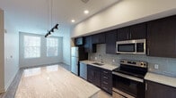 This single-floor unit showcases a contemporary design with a seamless open-concept layout connecting the kitchen, dining, and living areas. The kitchen is a standout feature, equipped with a full suite of stainless steel appliances, including a refrigerator, dishwasher, electric range, and built-in microwave. Rich, dark espresso cabinetry extending to the ceiling provides generous storage, while light granite countertops offer a striking contrast. A subway tile backsplash adds a refined finishing touch, and a large granite-topped kitchen island serves as a natural gathering point and workspace.

Recessed lighting and a sleek multi-head pendant track light illuminate the kitchen and dining area, while multiple windows allow natural light to brighten the living space. The floors throughout the main areas feature warm-toned hardwood-style planks, transitioning to light tile in the bathroom. The bathroom is well-appointed with a granite vanity top, dark cabinetry, a large mirror, and a tub-shower combination. Neutral wall tones and clean architectural lines give the entire space a modern, move-in-ready aesthetic.