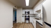 This single-floor residence offers a clean, modern aesthetic with thoughtfully updated finishes throughout. The kitchen serves as a standout feature, showcasing white shaker-style cabinetry, granite countertops, and a classic white subway tile backsplash. Stainless steel appliances — including a range, over-the-range microwave, and dishwasher — complement the space, while a stainless undermount sink with a gooseneck faucet adds a polished touch. Wood-look flooring runs through the kitchen and hallway areas, lending warmth and continuity.

A clean, well-lit hallway connects the main living areas to the private spaces, with louvered closet doors providing functional storage along the way. The bedrooms feature plush carpeting and neutral wall tones, with windows that invite natural light and offer views of the surrounding area. The bathroom continues the cohesive design language with granite-topped white vanity cabinetry, wood-look flooring, and a separate water closet with marble-style tile detailing. The overall layout, as suggested by the dollhouse view, provides a practical and open flow between the kitchen, living areas, and bedrooms, making this a comfortable and well-designed single-level living space.