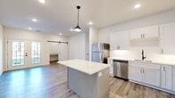 Located at 1200 S 44th St in Rogers, Arkansas, this one-bedroom, one-bathroom unit delivers a clean, contemporary design across a well-organized single-floor layout. Light wood-tone flooring runs throughout the entire space, creating visual continuity and a warm, cohesive feel.

The open-concept kitchen and living area form the heart of the unit. The kitchen is outfitted with white shaker cabinetry, quartz countertops, and a full suite of stainless steel appliances, including a refrigerator, dishwasher, microwave, and range. A central island with a quartz waterfall-style surface provides additional prep space and serves as a natural divider between the kitchen and living areas. A pendant light hangs above the island, complementing the recessed lighting overhead. A sliding barn door adds a modern farmhouse accent, leading to a dedicated closet or utility space.

The living area opens to the outdoors through a set of glass French doors, allowing natural light to fill the room. The bedroom offers a comfortable footprint with a ceiling fan, a large window with outdoor views, and direct access to the closet area. The bathroom features a white vanity with quartz countertops, a large framed mirror, and wood-look flooring consistent with the rest of the unit, all finished in a bright, neutral palette.