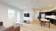 Located in Davis, CA, this modern 3-bedroom, 3-bathroom residence offers a clean, contemporary design across a single floor. The open-concept living and kitchen area serves as the heart of the home, featuring light wood-style flooring that runs throughout, recessed lighting, and a seamless flow between spaces. The living area includes a wall-mounted TV setup and direct access to a private balcony through a glass-paneled door, allowing natural light to fill the room. The kitchen is a standout feature, appointed with floor-to-ceiling matte dark cabinetry, white subway tile backsplash, stainless steel appliances including a refrigerator, range, microwave, and dishwasher, and a white countertop dining table with seating. Each of the three bedrooms is bright and well-proportioned, with light-toned walls, wood-style flooring, ceiling fans, and closet storage. The three bathrooms maintain a consistent modern aesthetic, featuring dark vanity cabinetry with white countertops, large mirrors, and tub-shower combinations with clean tile surrounds. Additional conveniences include an in-unit laundry area and multiple closets throughout. The overall ambiance is bright, minimal, and functional, ideal for comfortable everyday living.