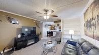 This efficiently designed one-bedroom, one-bathroom unit offers a thoughtful layout across a single floor, making excellent use of its compact footprint. The living room serves as the heart of the space, featuring plush carpeting, crown molding, a textured ceiling, and a ceiling fan with light fixture. Built-in shelving adds both functionality and character, while the open sightline connects seamlessly to the combined dining room and kitchen area. The kitchen is well-equipped, featuring warm wood cabinetry, granite-style countertops, a full suite of black appliances including a stainless range, microwave, and refrigerator, and tile flooring. A dedicated pantry provides additional storage. A hallway connects the main living areas to the private bedroom, which offers carpet flooring, crown molding, a ceiling fan, and access to two closets for ample storage. The bathroom is finished with a wood vanity, granite-style countertop, a large mirror with overhead lighting, and tile flooring. Throughout the unit, consistent use of crown molding, neutral tones, and warm accent walls creates a cohesive and comfortable living environment.