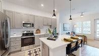 This thoughtfully designed 2-bedroom, 2-bathroom single-story residence offers a seamless open-concept layout that connects the kitchen, dining, and living areas into one cohesive, light-filled space. The kitchen is a standout feature, showcasing gray shaker-style cabinetry, a classic white subway tile backsplash, quartz countertops, and a full suite of stainless steel appliances. A generous center island with seating serves as both a functional workspace and a natural gathering spot, illuminated by stylish pendant lighting overhead. Light wood-tone flooring flows throughout the main living area, complementing the bright, neutral palette. The living room is bathed in natural light from large windows dressed with white plantation shutters, creating a welcoming and airy ambiance. Both bedrooms are carpeted and feature large windows with outdoor views, providing a serene retreat. The primary bedroom offers a comfortable sense of scale with generous closet space. Each bathroom is well-appointed, with one featuring a sleek glass-enclosed walk-in shower with white subway tile. Two dedicated closets add practical storage throughout. The overall design balances modern finishes with a warm, inviting atmosphere.