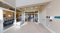 The Brio at The Boulevard, located at 410 Princeton Road in Yaphank, NY, presents a thoughtfully designed two-floor clubhouse and amenity center built to serve its residential community. The entry foyer sets an immediate tone of sophistication, featuring large-format light tile flooring, soaring double-height ceilings, and expansive floor-to-ceiling glass doors that flood the space with natural light while offering views of the surrounding grounds.

Beyond the entryway, warm hardwood flooring extends throughout the main level, connecting a series of well-appointed spaces. A comfortable lounge area provides stylish seating for socializing, while a dedicated game room features a poker table beneath a striking sculptural chandelier, nautical-themed artwork, and an arcade game — ideal for casual entertainment. Built-in shelving with cabinetry adds functional elegance to the common areas.

The fitness center is generously sized, equipped with modern cardio machines including treadmills and stationary bikes, and benefits from large windows overlooking the community's outdoor spaces. Adjacent to the gym, a dedicated yoga and barre studio features floor-to-ceiling mirrors, a wall-mounted ballet barre, and ceiling fans, providing an ideal environment for group fitness.

Upper-level seating nooks with leather chairs, tray ceilings, and arched windows offer quiet retreats, rounding out a clubhouse designed for both activity and relaxation.
