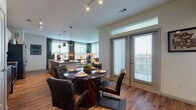 This single-story, two-bedroom, two-bathroom residence offers a thoughtfully designed open-concept layout with modern finishes throughout. Wood-style flooring runs through the main living areas, complementing the warm, contemporary aesthetic of the space.

The kitchen features a galley-style configuration with dark lower cabinetry, white upper cabinets, granite countertops, stainless steel appliances, and pendant lighting overhead. It opens directly into the dining area, which benefits from large windows and a glass door that invite abundant natural light and outdoor views.

The living room is bright and welcoming, with oversized windows framed by floor-length drapes, creating a comfortable and airy atmosphere.

A hallway connects the two bedrooms, each carpeted and featuring large windows with exterior views. Both rooms offer ample space and a calm, restful ambiance.

Each bathroom is finished with wood-style flooring, white cabinetry, granite countertops, and large mirrors above the vanities. One bathroom includes a soaking tub, adding a refined touch to the overall design.

The residence combines functional layout with cohesive, modern design elements, making it a well-balanced and inviting living space.